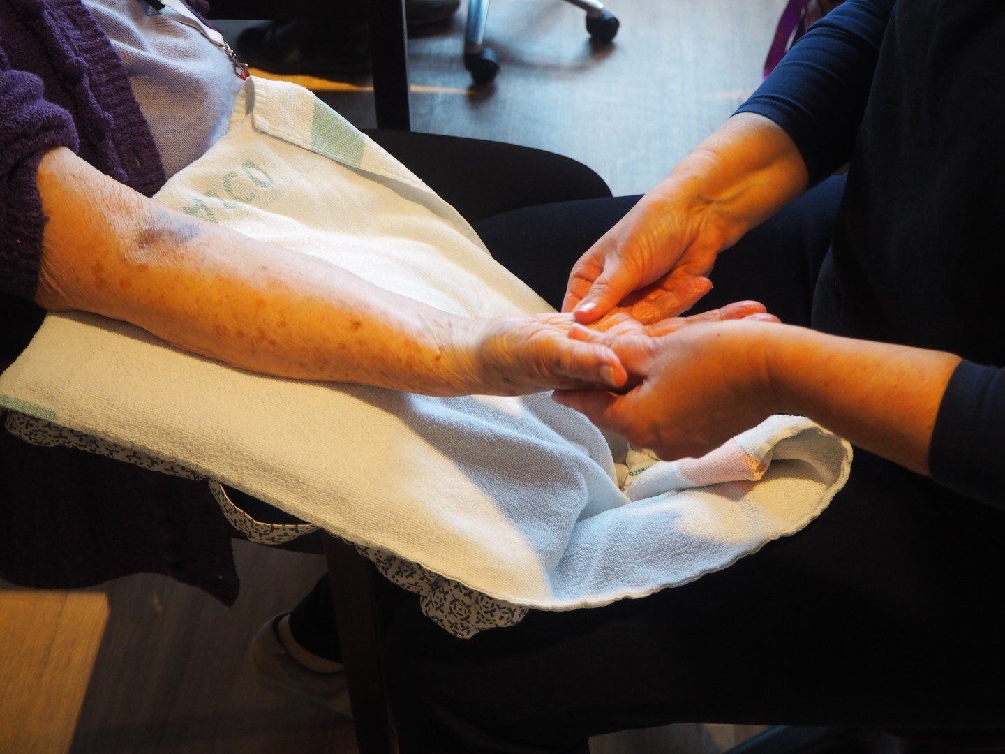 Een vrijwilliger masseert de hand en onderarm van een oudere vrouw, die op een handdoek op haar schoot rusten